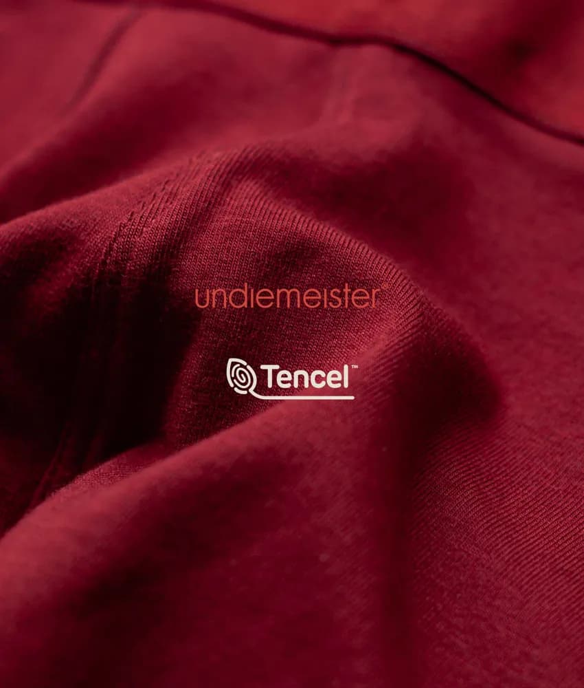 Close-up van de Mellowood stof in donkerrood met het Undiemeister- en TENCEL-logo
