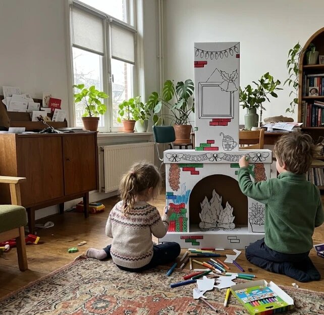 Twee kinderen kleuren samen de kartonnen open haard van Bankers Box Play in de woonkamer